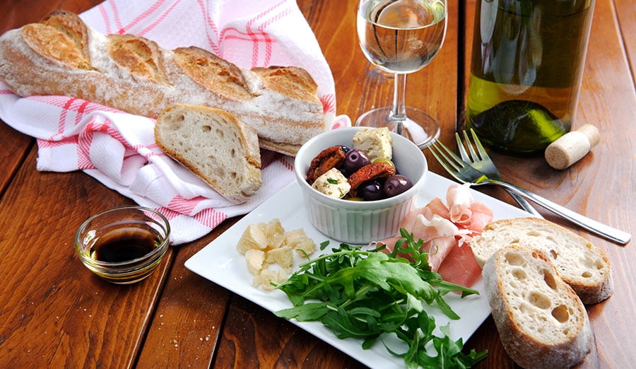 spread of bread, cheese and vegetables with a glass of white wine