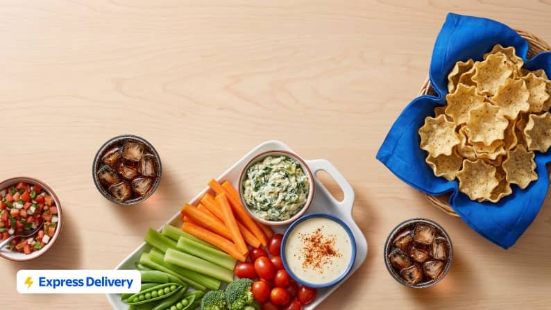 A vegetable tray, a bowl of pico de gallo, a bowl of tortilla chips, and two iced beverages.