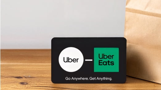 An image of an Uber and Uber Eats gift card next to a paper bag on a wood table.