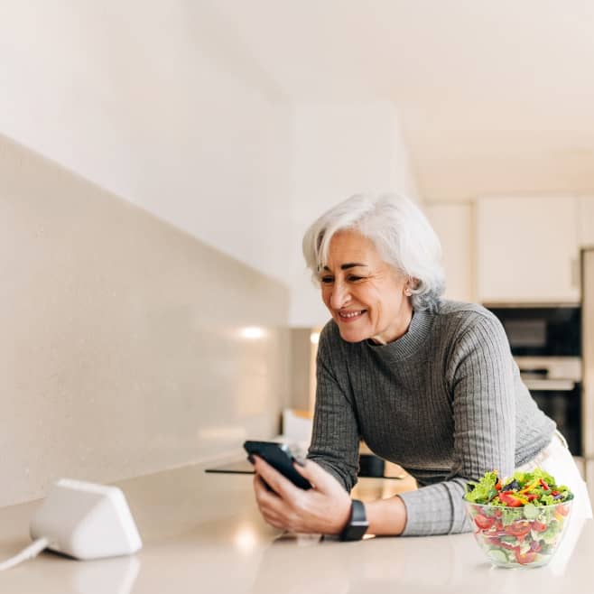 Older woman sitting at a table and looking at a smartphone.