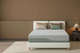 View an unmade mattress with neutral colors and four pillows on it.