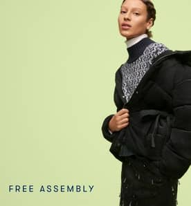 Woman in a black puffy jacket over a white and navy mock neck sweater, white turtleneck, and beaded black skirt.