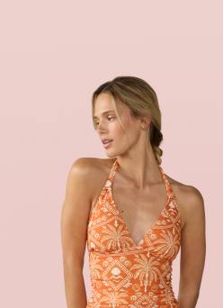 Woman in an orange patterned one-piece swimsuit posing against a soft pink background.