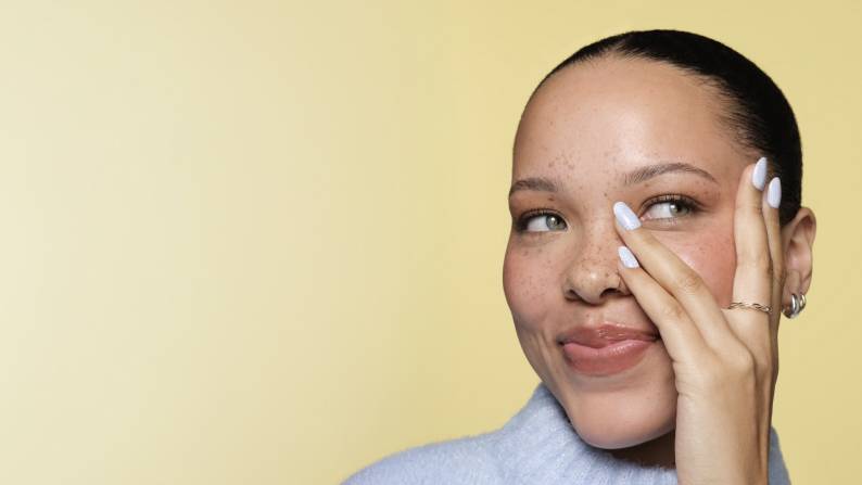 Woman posing with floral manicure, hand near face, on yellow background with text “Pastel nails for spring” and “Shop now”.