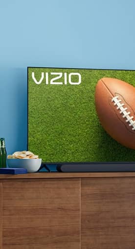 A big screen TV displays a football on the field and snacks on the TV stand.