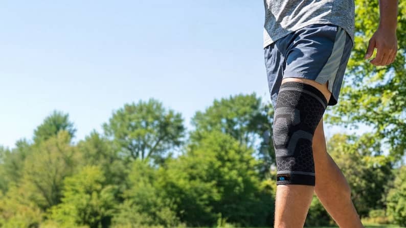 Active man outside surrounded by trees using knee brace.