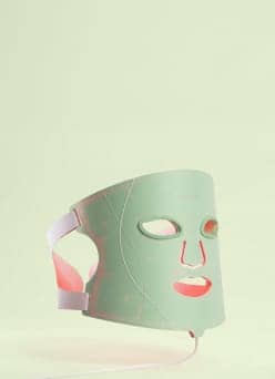 Mint green LED face mask with eye and mouth openings, side straps, and a cord, shown against a pale green background.