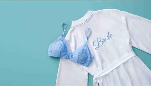 A white robe with Bride embroidered on back and a blue bra are pictured on a blue backdrop.
