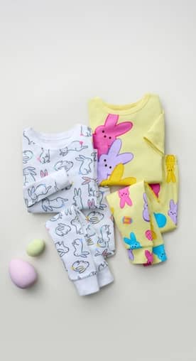 A set of white, bunny-printed pajamas and a set of colorful Peeps pajamas are surrounded by colorful eggs.