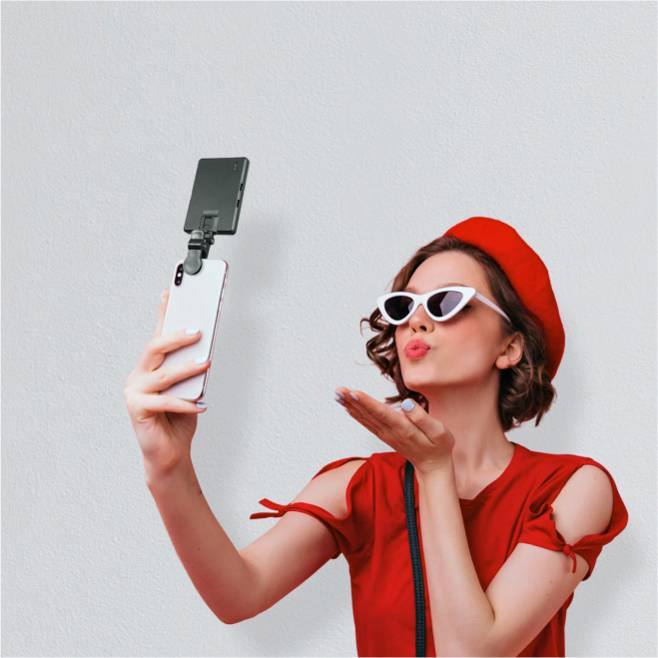 Image of a woman wearing a red hat and shirt taking a selfie with a smartphone that has a flip-up attachment.