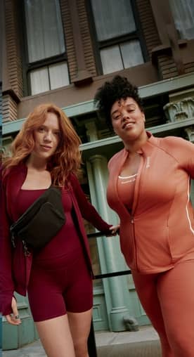 Two young women are pictured standing in front of a building wearing workout tanks and zip-up jackets from top brands like Avia and Reebok.