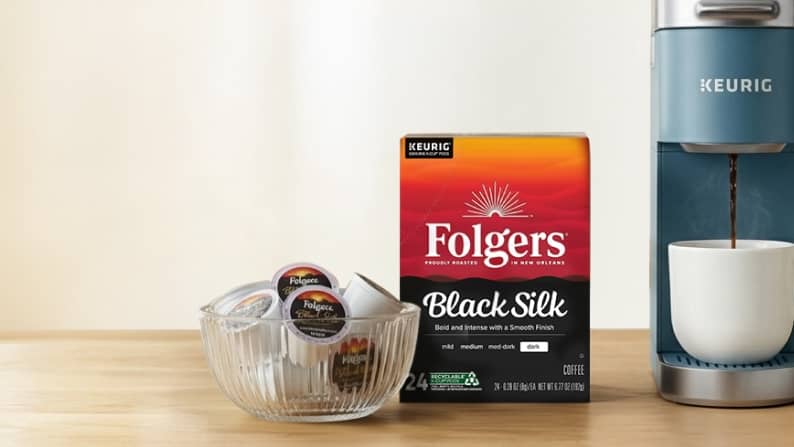 A box of Folgers black silk coffee pods next to a Keurig machine.