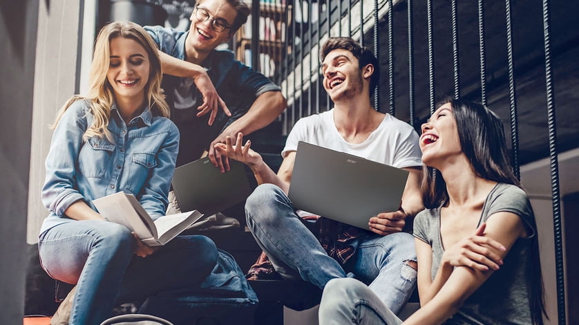 A group of people sitting in a stairwell joyously laughing while holding Acer laptops and a book.