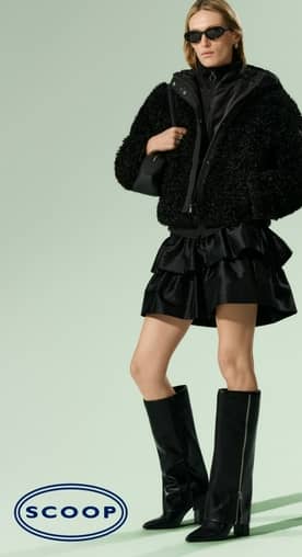 Model in black textured faux fur teddy jacket over black outfit with tiered mini skirt, knee-high boots, sunglasses and small black handbag.