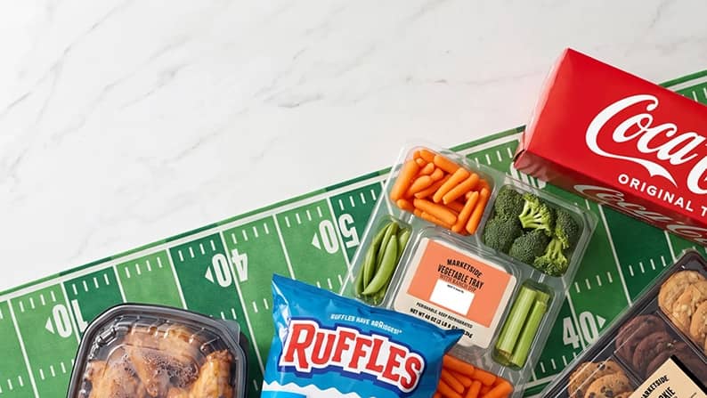 Coca Cola box, Ruffles chips, Marzetti vegetable dip tray, cookies and roasted chicken on a football field yard line table.