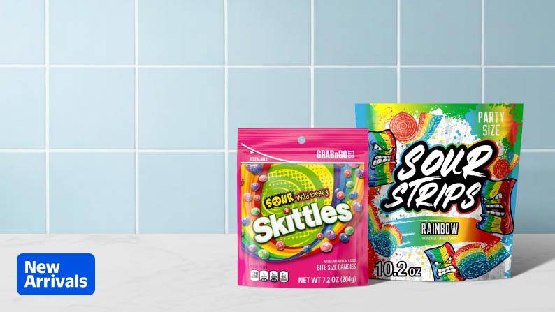 A bag of Sour Wild Berry Skittles next to a bag Rainbow Sour Strips over a white marble countertop.