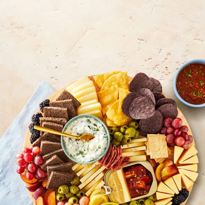 A platter of chips, cheeses, crackers, fruits, meats, and dips is shown.