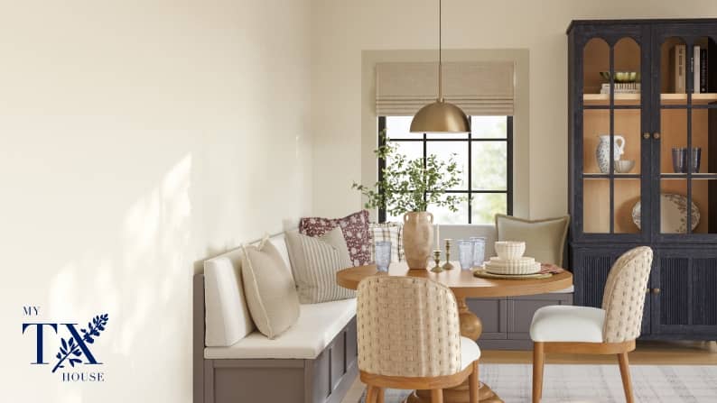 A cream dining nook with upholstered bench seating, wood table, upholstered chairs and a sage hutch.