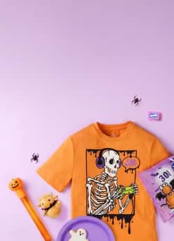 Orange kids T shirt with skeleton gamer graphic and Halloween toys, candy and plates with ghost and pumpkin designs.