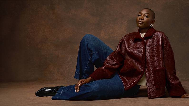 A woman is shown wearing a merlot red faux shearling button-up jacket with two front faux shearling pockets.