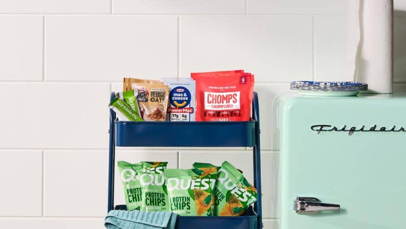 A shelf featuring a variety of protein snacks next to a minifridge.