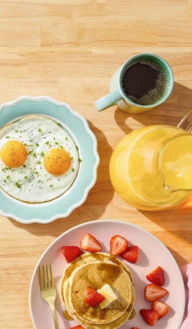 A brunch spread is shown complete with fruit-topped pancakes, fried eggs, orange juice and coffee.