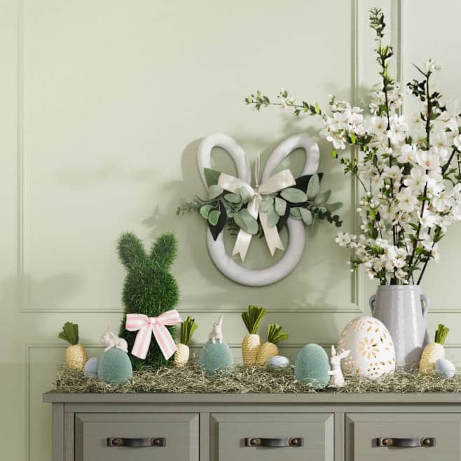 Entryway table with textured bunny and egg ornaments along with flowers and wreaths in green, blue and yellow.