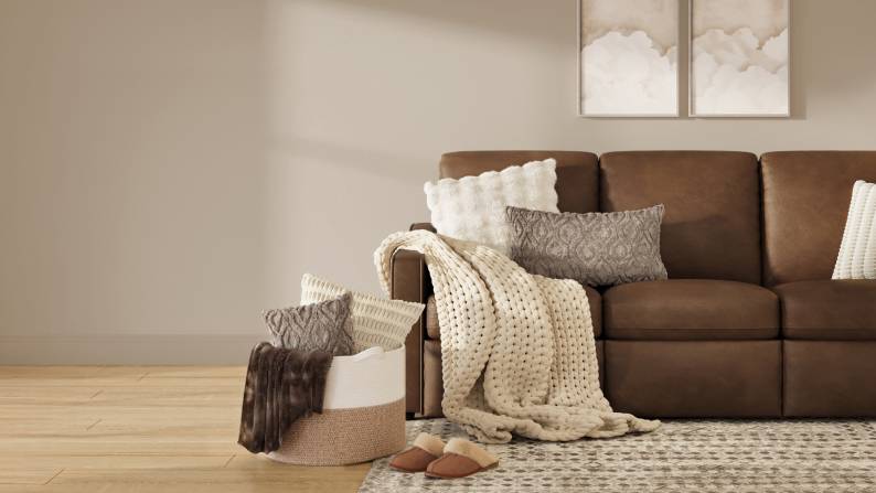 A mix of neutral throws is seen with a brown sofa, rug, and cozy slippers in a taupe room.