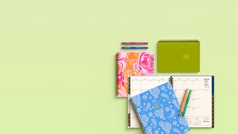 Pink, green, and blue notebooks on a green background.