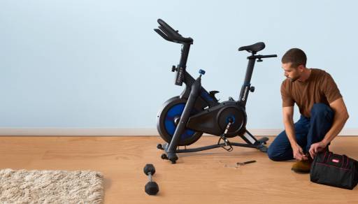 An image of a person kneeling in front of an exercise bike.