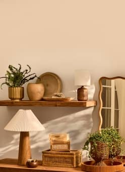 Wooden floating shelves are styled with woven baskets, potted plants, a pleated lamp and various wood and wicker decorative objects.