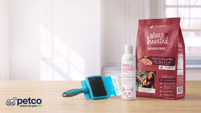 Petco where the pets go. Whole Hearted Grain Free pet food bag with Well Good spray and blue grooming brush on a light surface.
