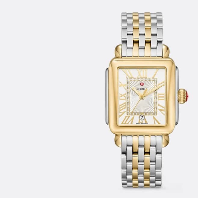 Silver and gold Michele watch is pictured on a light grey backdrop.