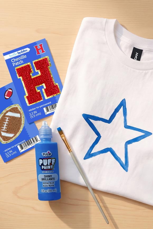 White t shirt with a blue star painted on it. Blue puff paint and a paint brush, football chenille patch and letter H chenille patch.