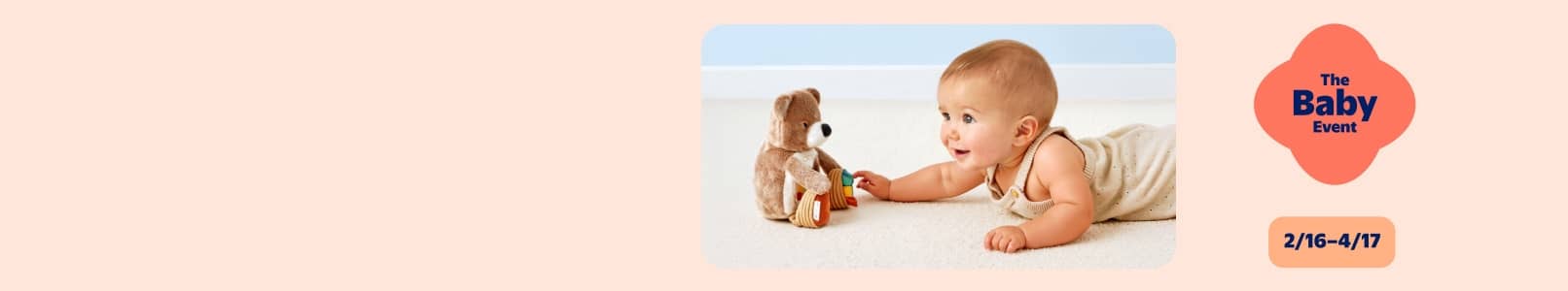 A baby crawling on a white carpet toward a plush teddy bear toy. The Baby Event and 2/16-4/17