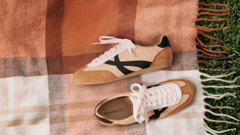 Pair of tan and cream suede sneakers with black accents displayed on a plaid picnic blanket.