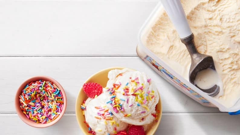 A bowl of vanilla ice cream with sprinkles and cherries next to a pint of ice cream.