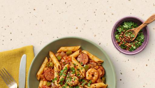 A plate of pasta is shown, topped with sausage, shrimp & seasonings.