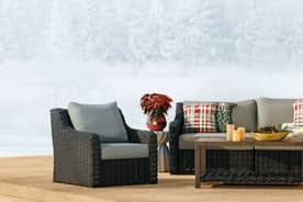 An image of grey patio furniture on a wood deck, decorated with string lights and plaid pillows, flowers, and candles.