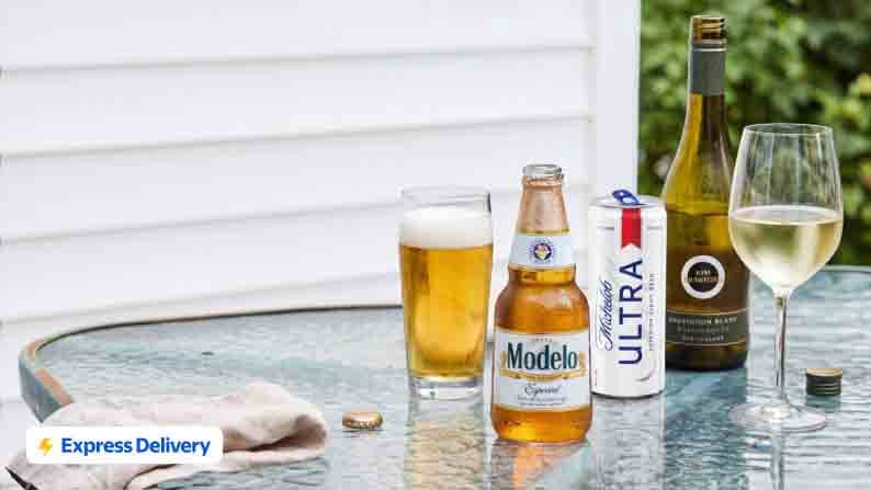 A can of Modelo, Michelob Ultra and a bottle of wine are shown on an outdoor table. Featuring a cup of poured beer and poured wine.
