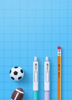 Pens against a blue grid, next to a small soccer ball and a small football.