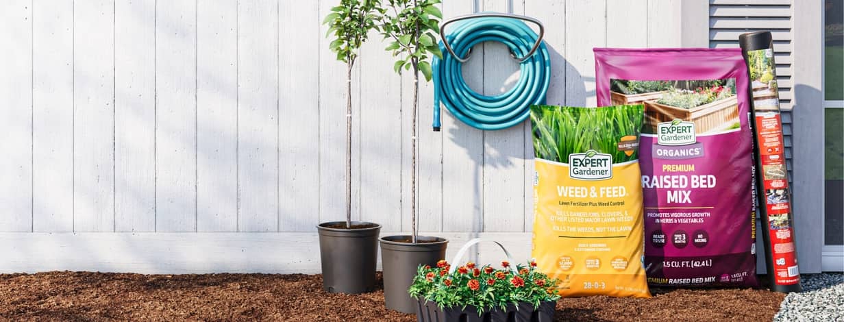 Expert Gardener logo. Weed and feed bag, soil bag, flowers and small trees in pots with a blue garden hose.