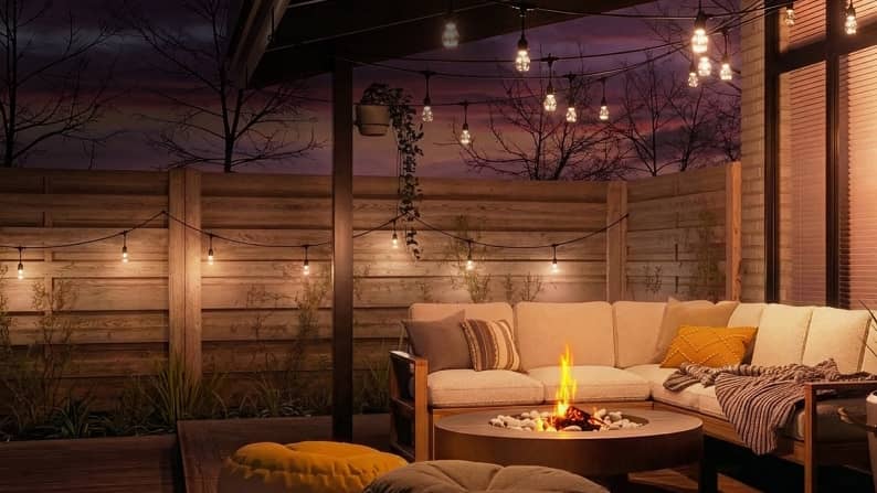 Outdoor patio at night featuring sectional sofa, cushions, firepit and lit string lights.