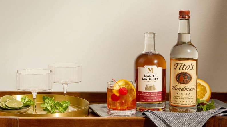 A mixed cocktail next to a bottle of Master Distillers bourbon and Tito’s vodka.