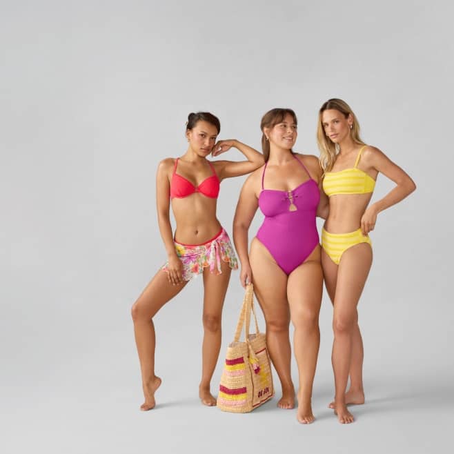 Three women wearing colorful swimwear are standing together.