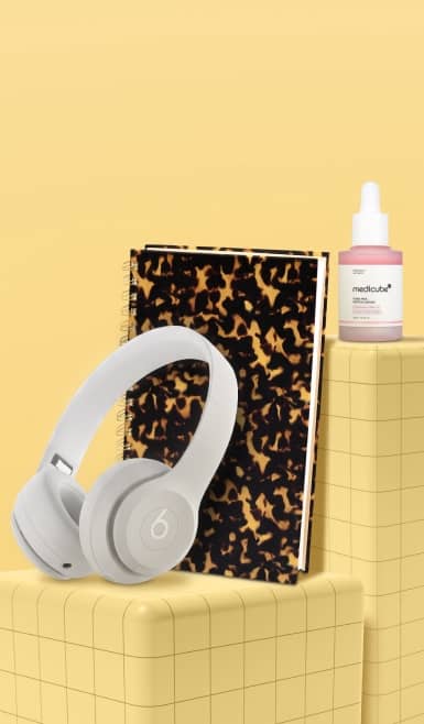 Beats headphones, patterned notebook and Medicube serum on yellow background.