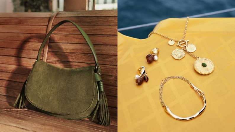 Olive green shoulder bag with tassel details on a wooden bench beside layered gold necklaces, hoop earrings and bracelets.