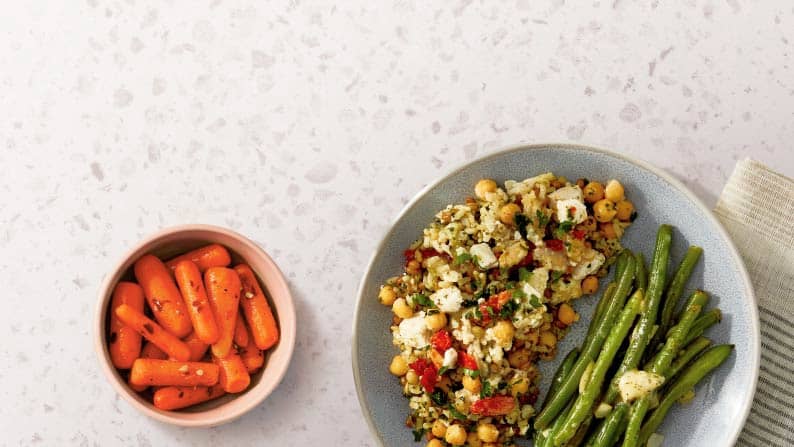 A plated dinner is shown on a counter, including a plate of skillet rice mix, grilled asparagus and a side of cooked carrots.