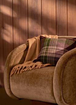 Cozy armchair with a plaid pillow and a folded throw blanket draped over the side.