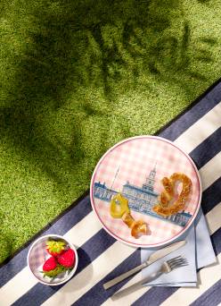 Gingham plate and bowl with Philadelphia motif shown on blue and white striped picnic blanket over grass.